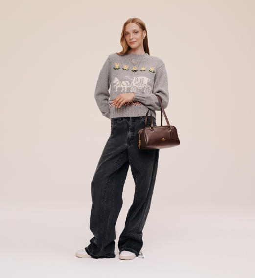 Woman wearing brown teddy jacket, black leather A-line skirt, and carrying a brown handbag.